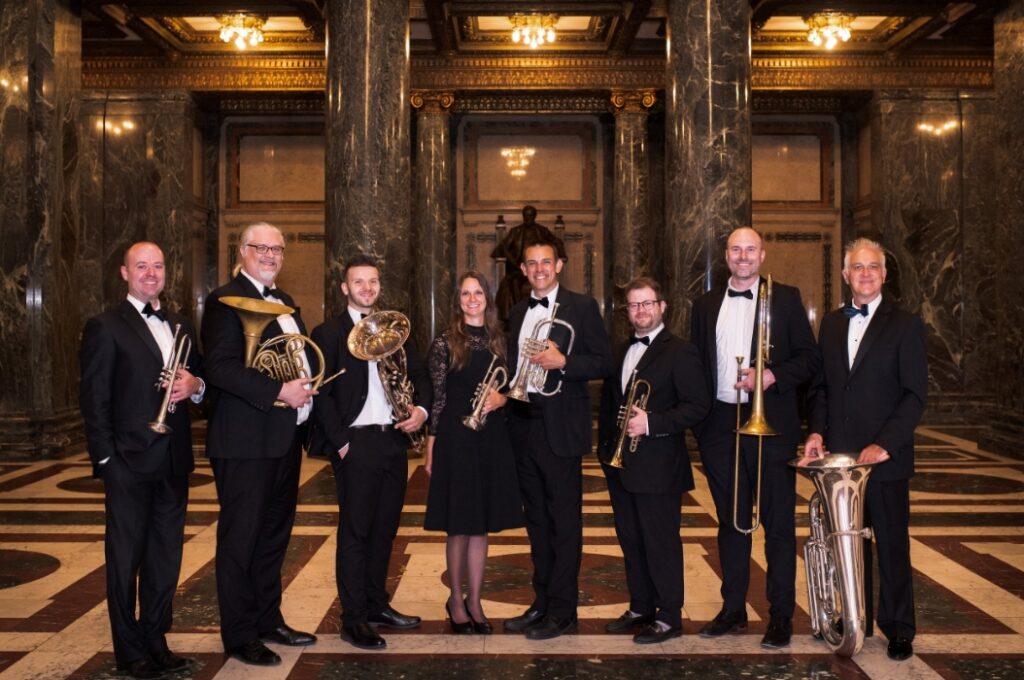 8 musicians in grand hall holding instruments