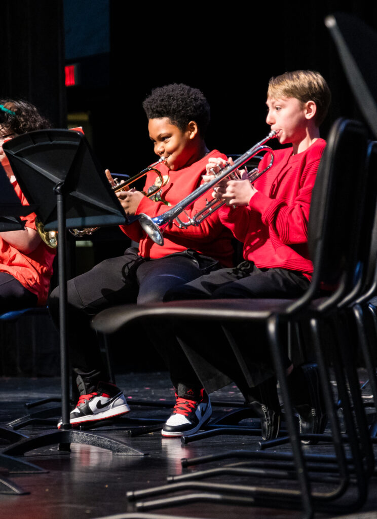 Two male students play the trumpet on stage, their music stands are in front of them.