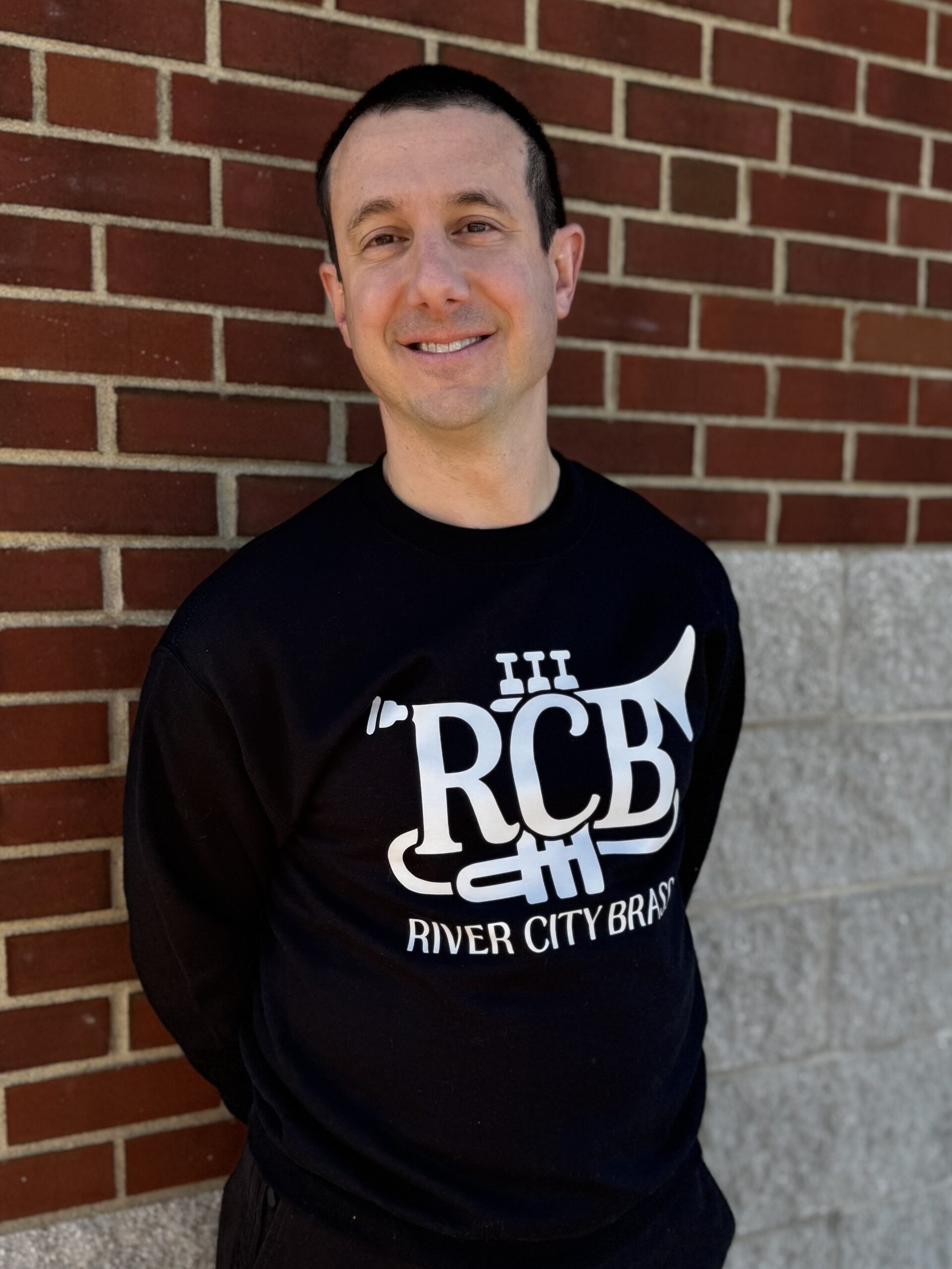 RCB Black Crewneck Sweatshirt, modeled by a member of the band in front of a brick wall